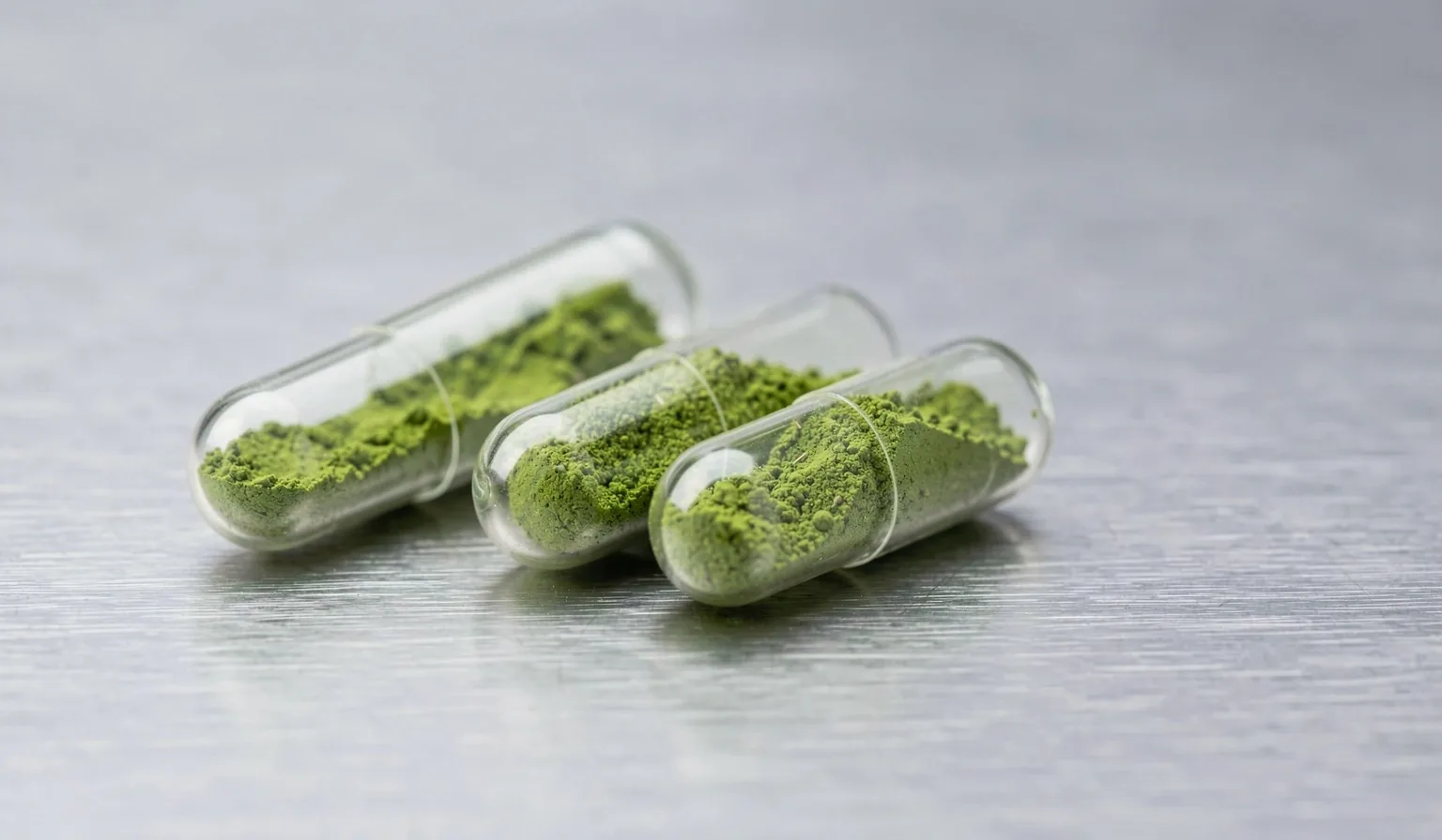 Clear capsules with green botanical powder on steel surface